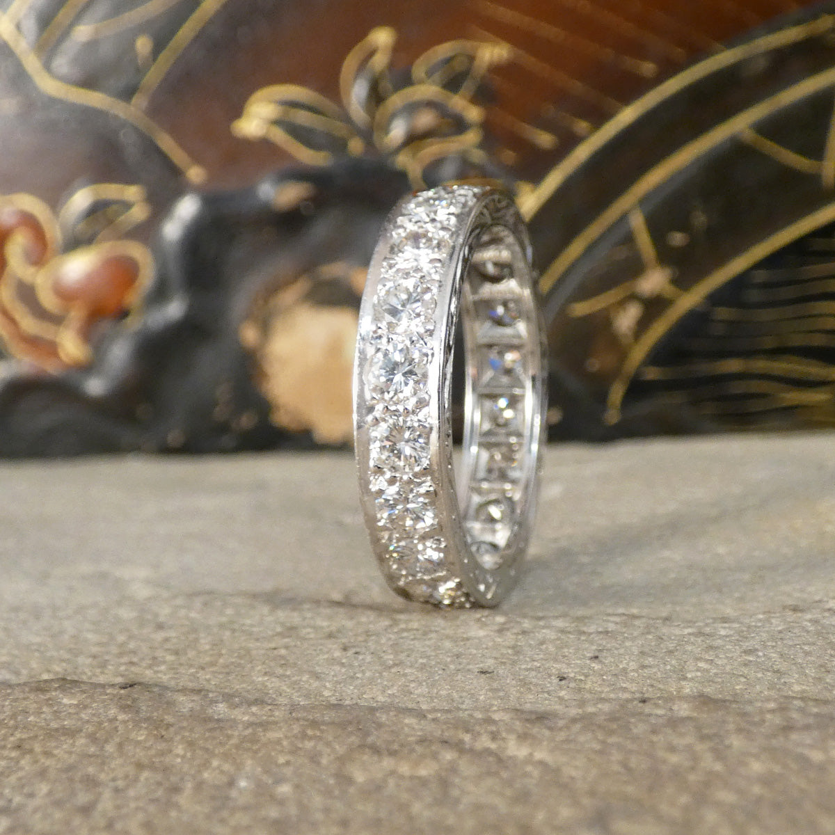 A full diamond eternity ring in 18ct white gold. Displayed on an ornate background showing the front and behind the back 