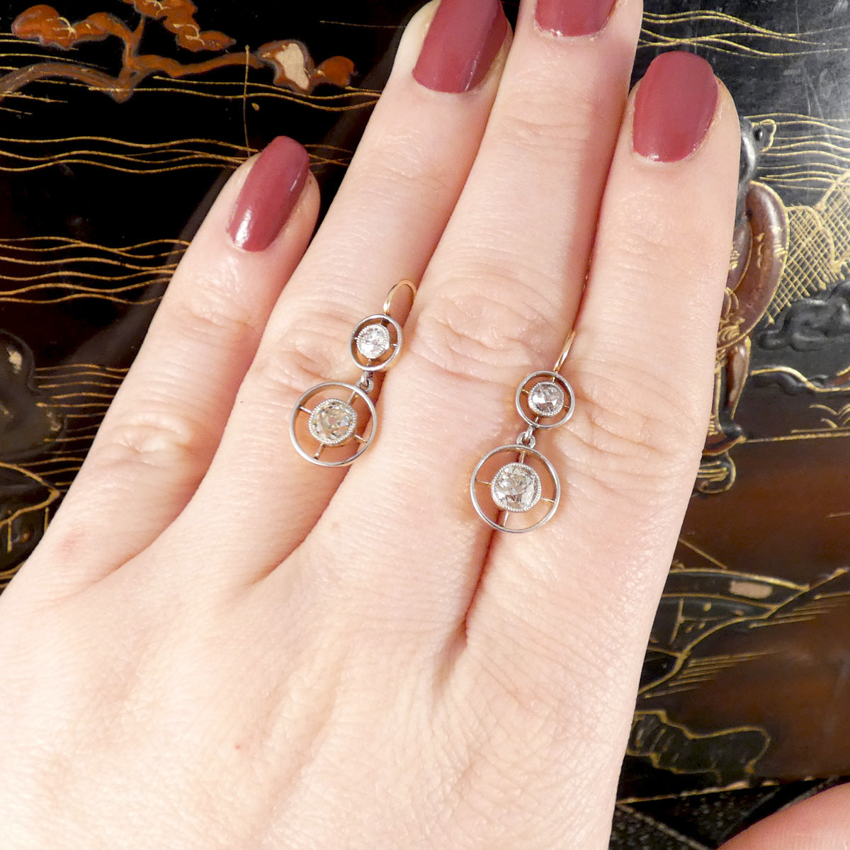 platinum and gold earrings with circular design worn on a hand against an ornate background