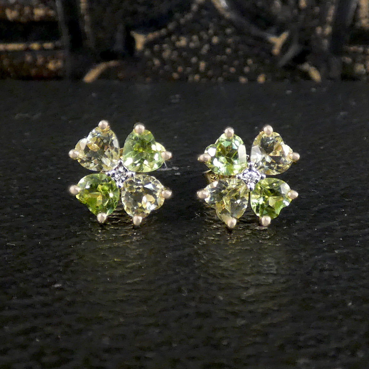 A pair of yellow gold stud earrings with four green gemstones arranged in a clover shape, on a dark surface.
