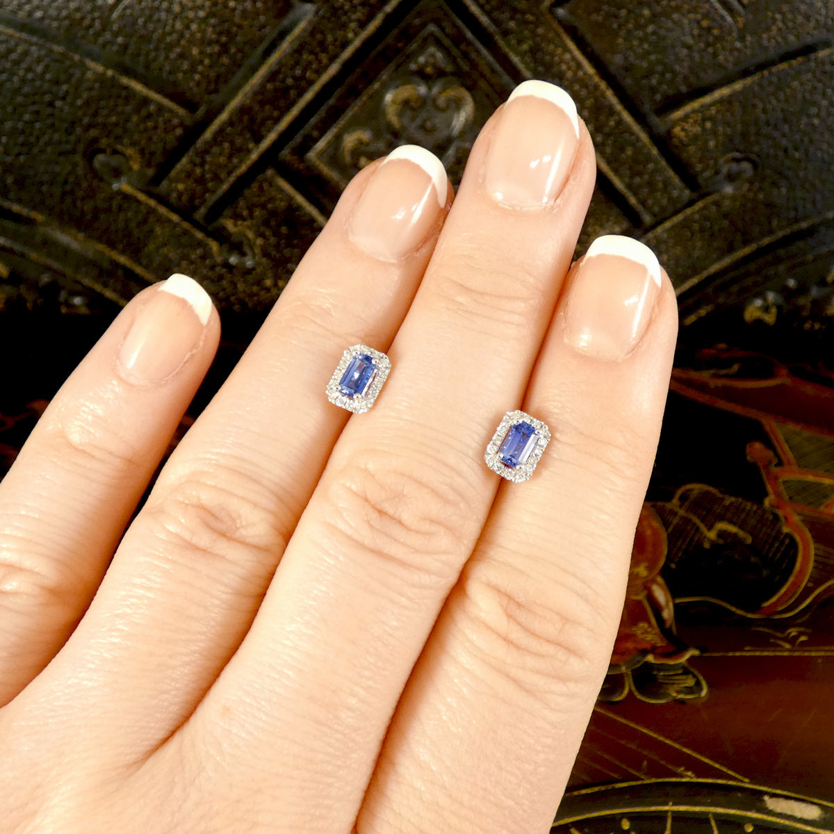 A pair of Emerald Cut bright Sapphire and Diamond cluster earrings in 18ct white gold. Displayed on the hand to see size and colour reference.