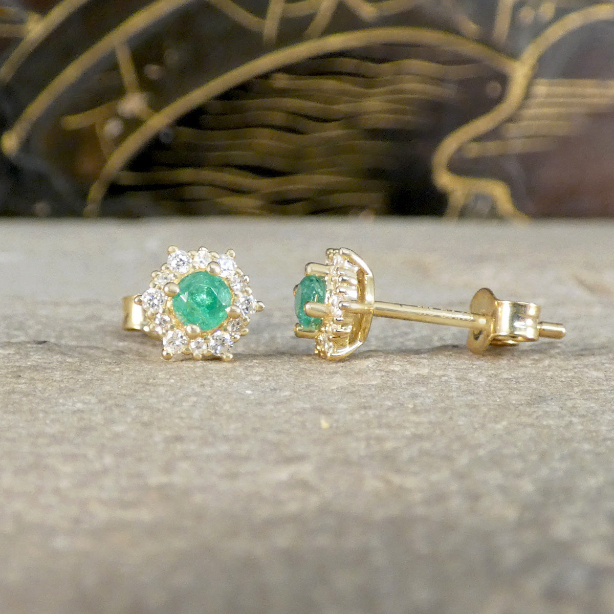 Gold earrings with emerald stones on a textured surface