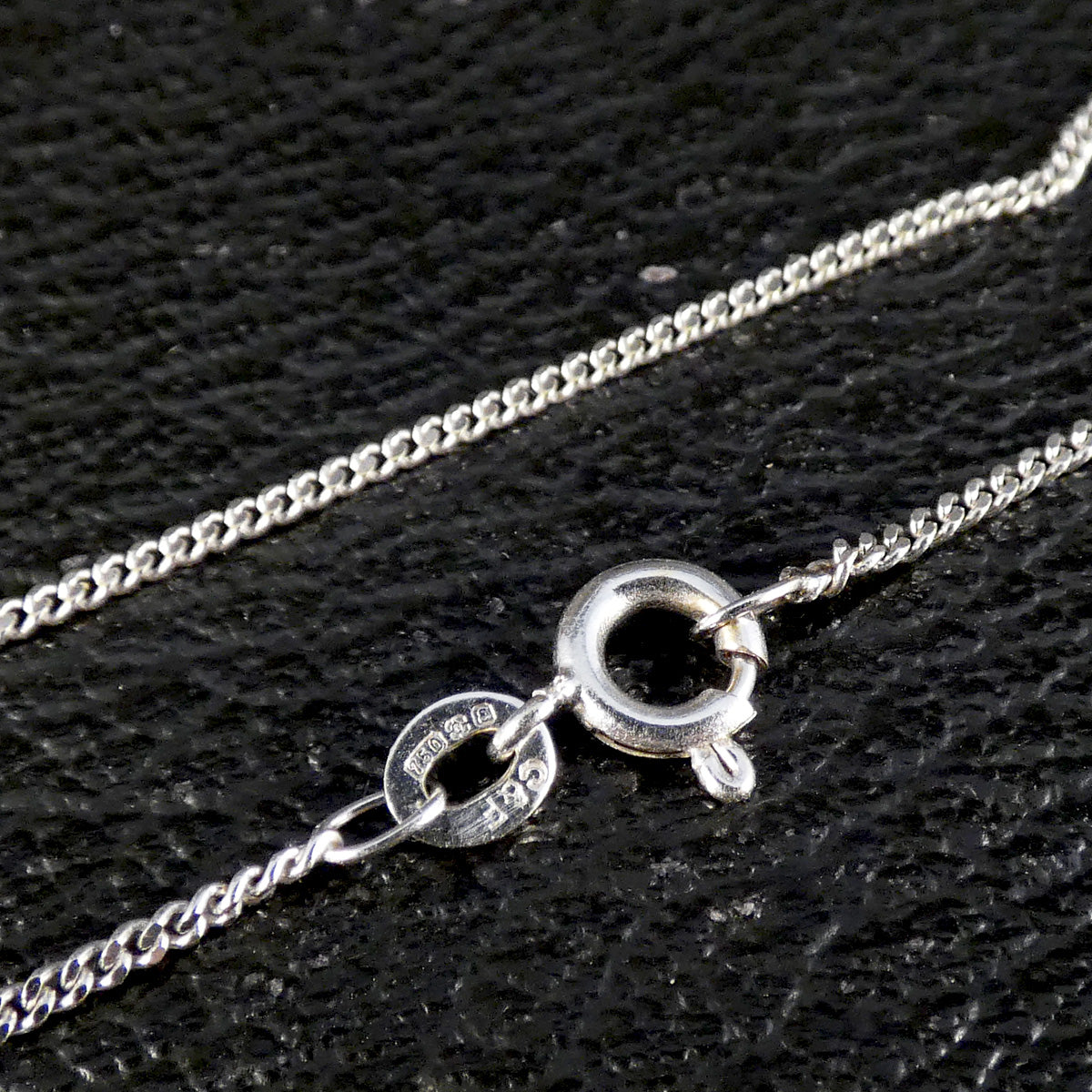 Bolt ring on a curb chain in 18ct white gold showing hallmarks on a dark background