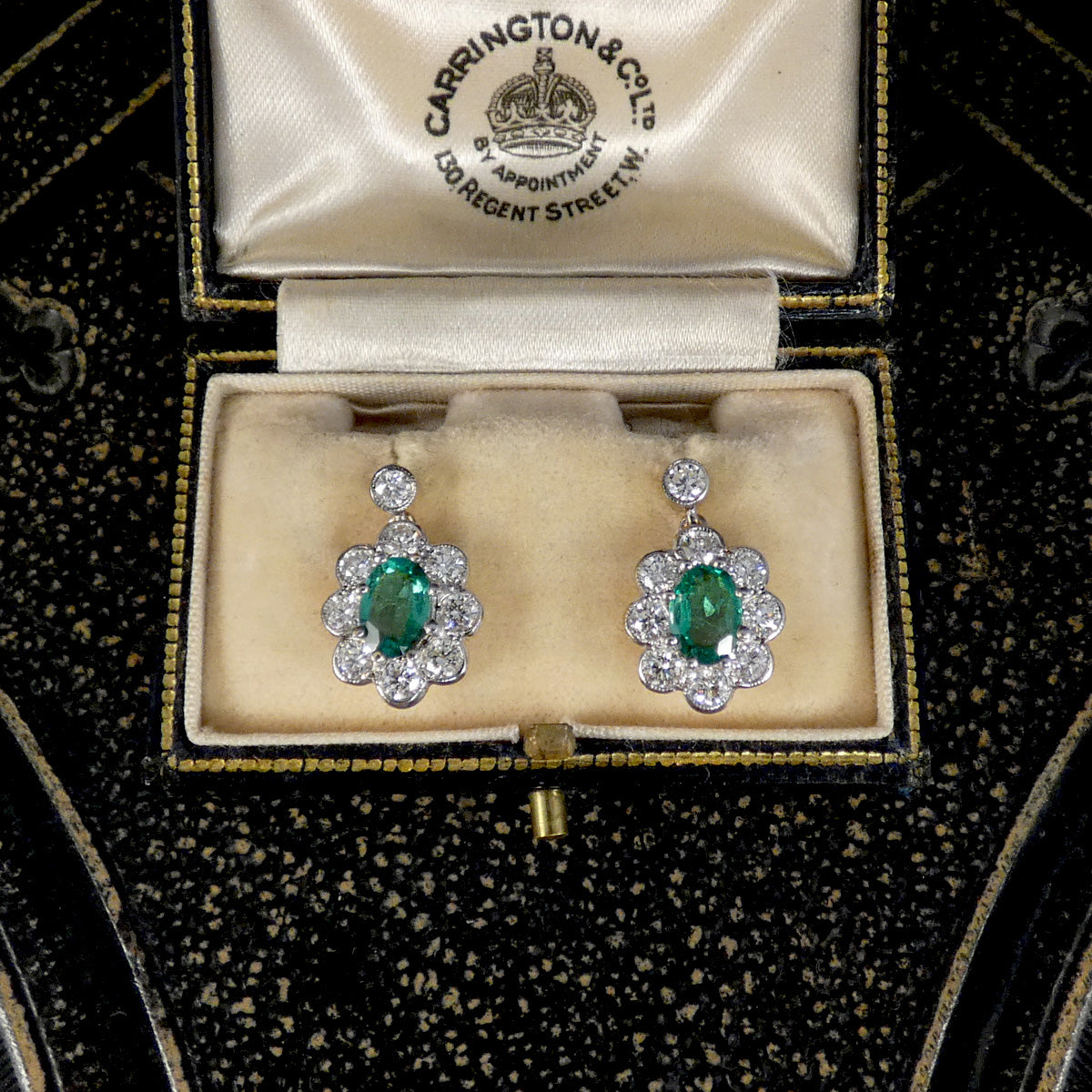 A pair of vintage Carrington & Co. emerald-cut green gemstone dangle earrings set in white and yellow gold with diamonds, presented in an open cream velvet jewelry box.