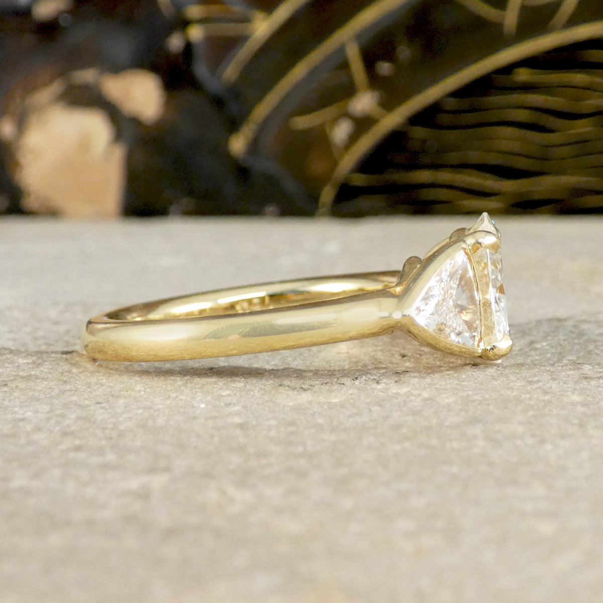 Gold engagement ring with a triangular diamond on a textured surface