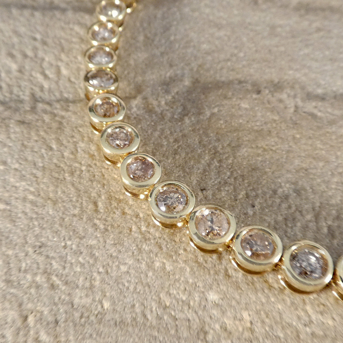 champagne diamond tennis bracelet with full rub over bezel settings.