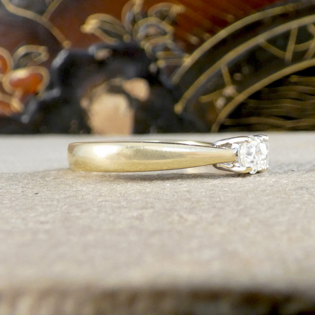 Gold ring with a diamond on a textured surface with a decorative background