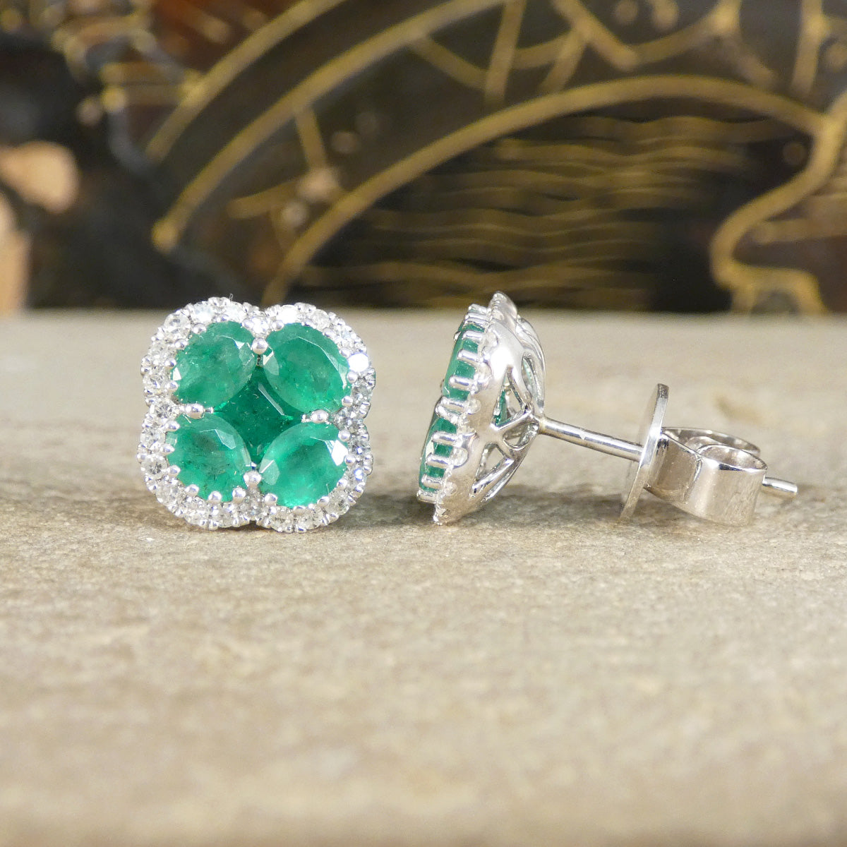 Pair of emerald earrings on a textured surface with a blurred decorative background