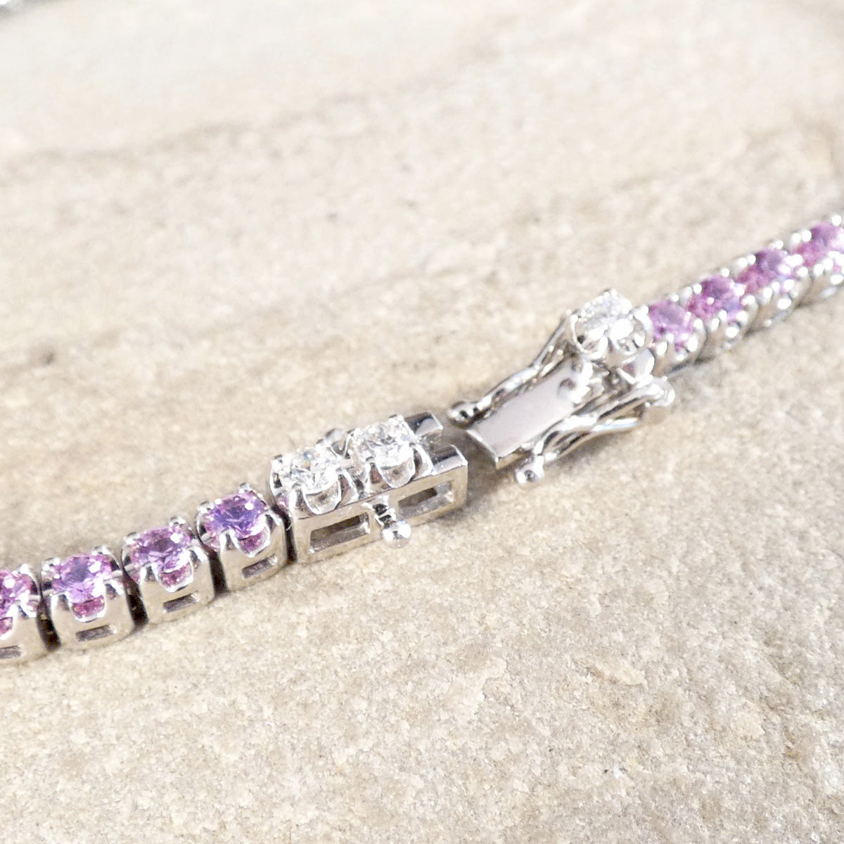 A snap lock set with diamonds and a figure eight lock on a  pink sapphire and diamond tennis bracelet in white gold