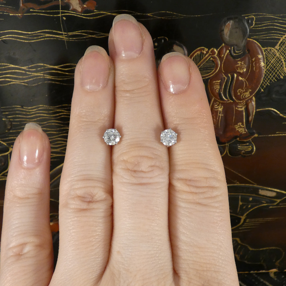 Diamond stud earrings on a hand with a decorative background