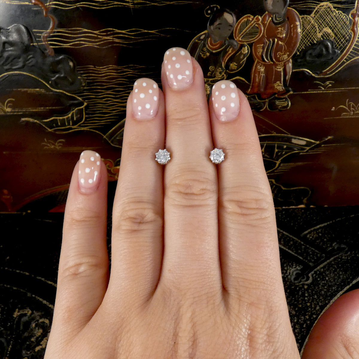 Hand wearing diamond stud earrings with a decorative background
