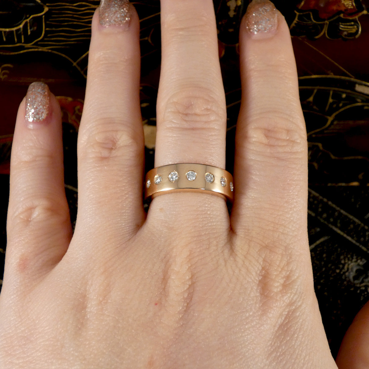 A diamond set rose gold band shown on the finger.