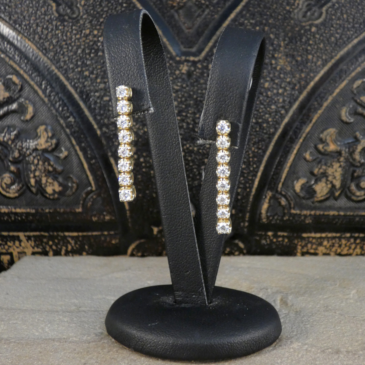 a pair of diamond drop earrings displayed on an earrings stand to show the drop