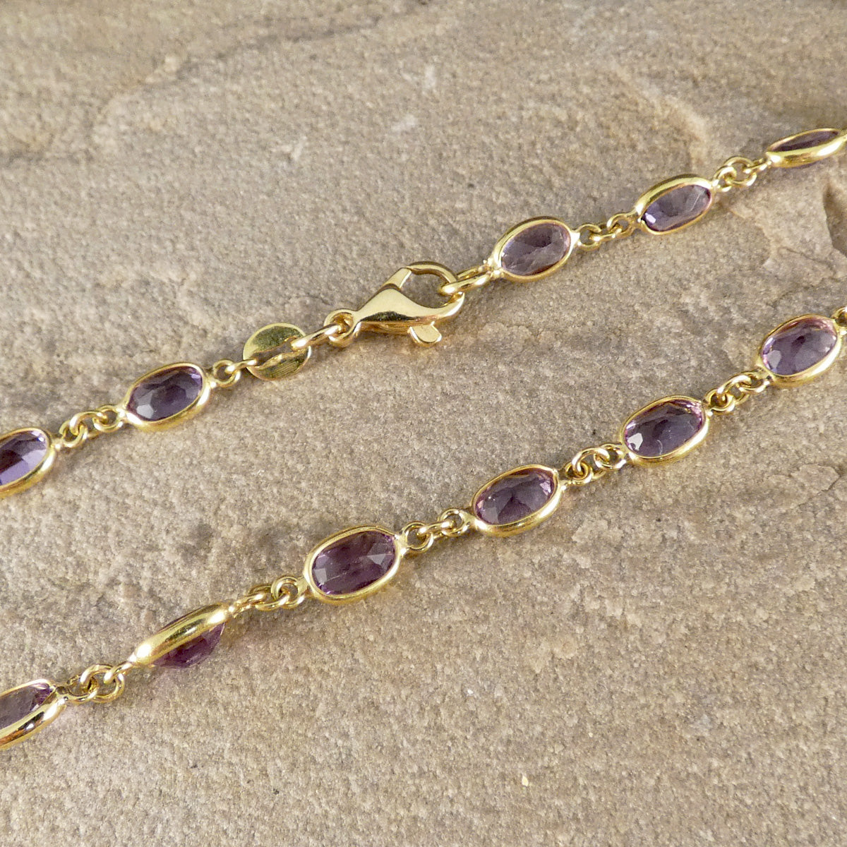 Gold bracelet with purple gemstones on a beige surface
