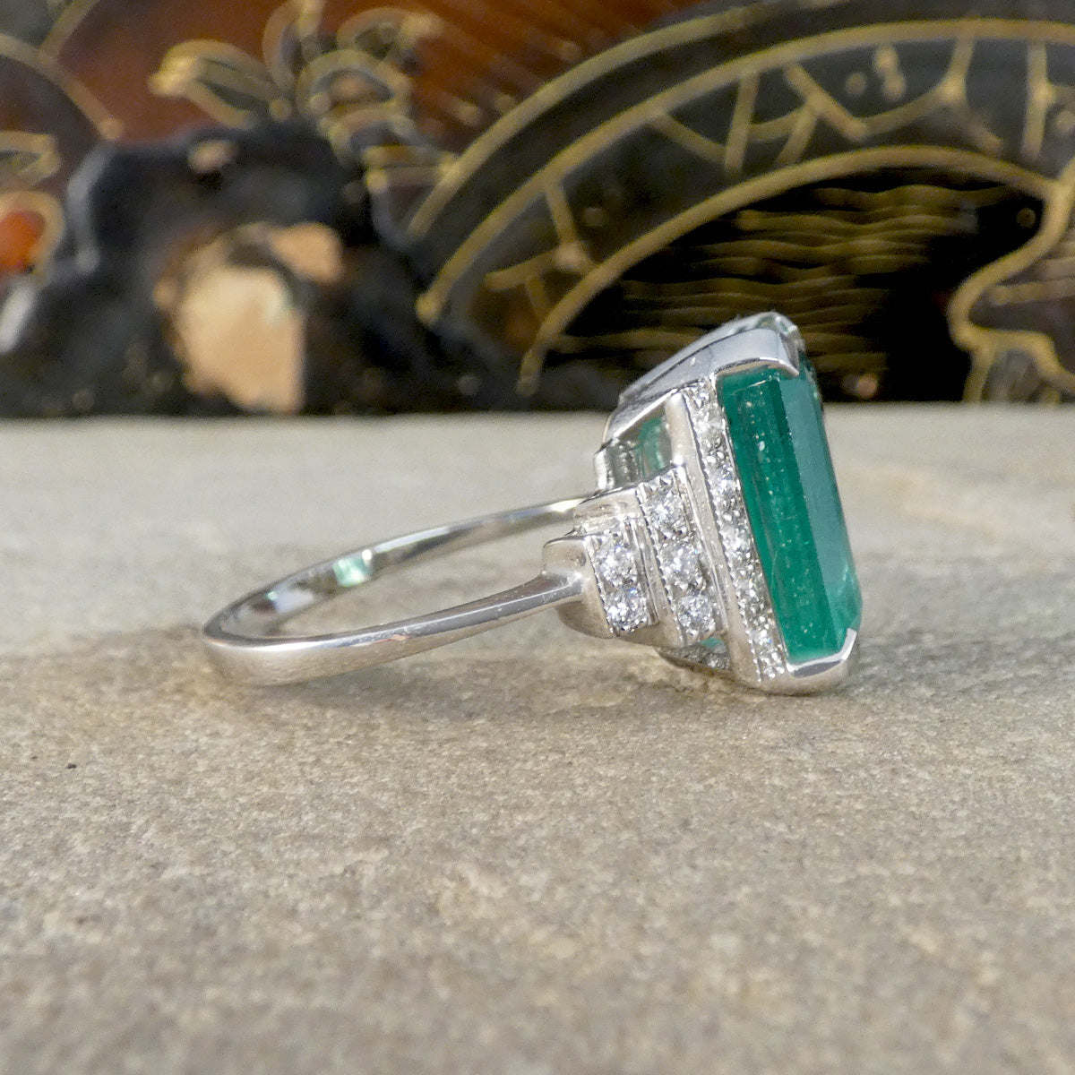 Side profile of Emerald and Diamond ring showing staged diamond set shoulders with a milgrain edge all set in Platinum.