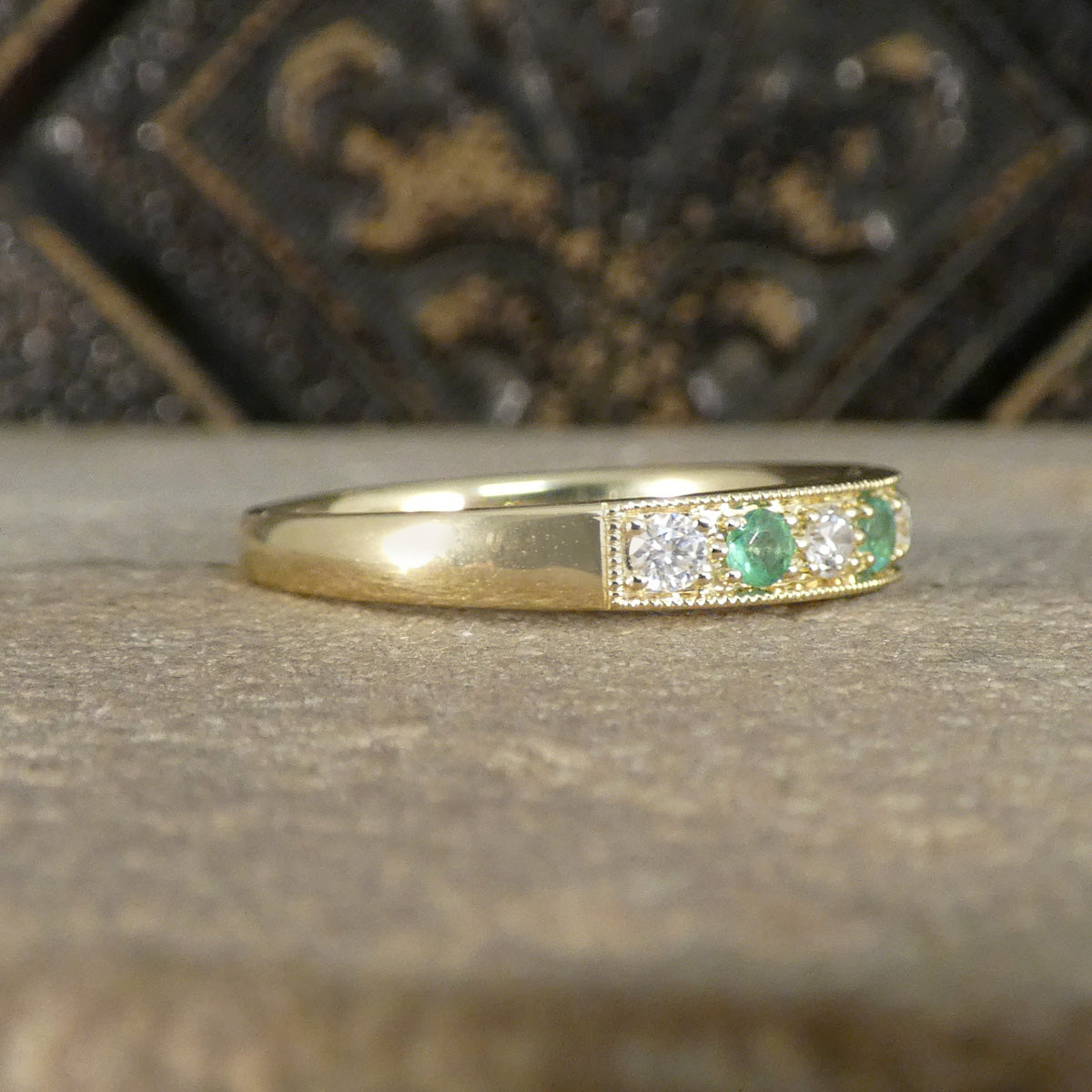 Gold ring with emeralds and diamonds on a textured surface