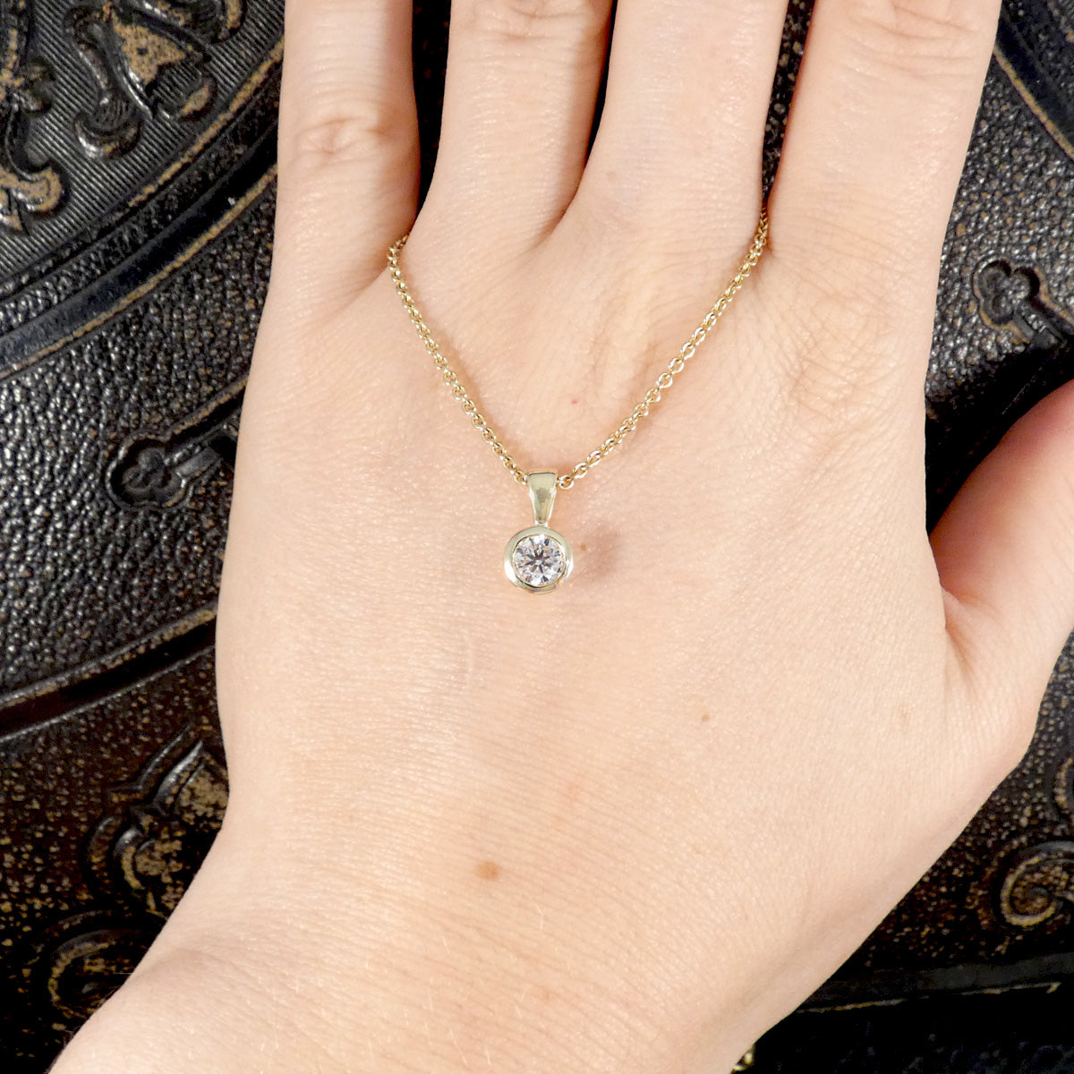 Gold necklace with a diamond pendant on a hand against a decorative background