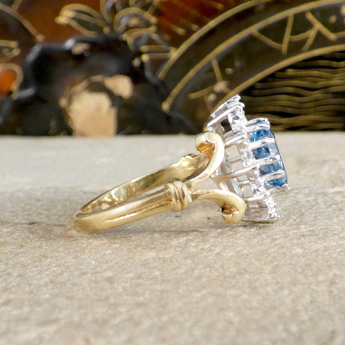 Gold ring with diamond and blue gemstone on a textured surface