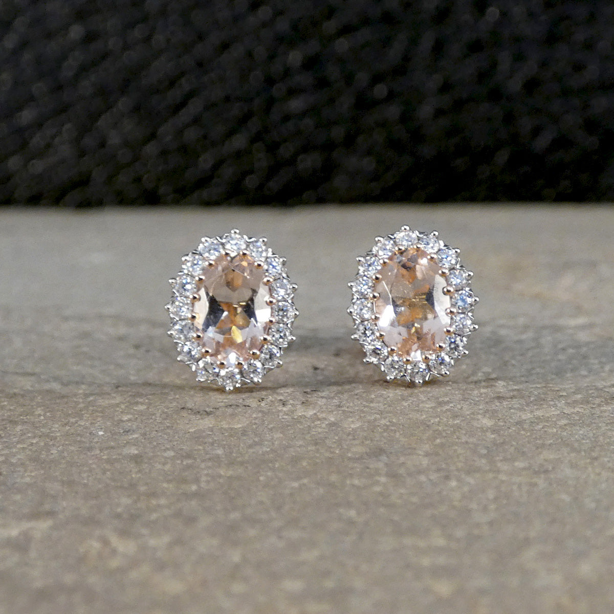 Pair of rose gold earrings with peach-colored gemstones on a neutral background
