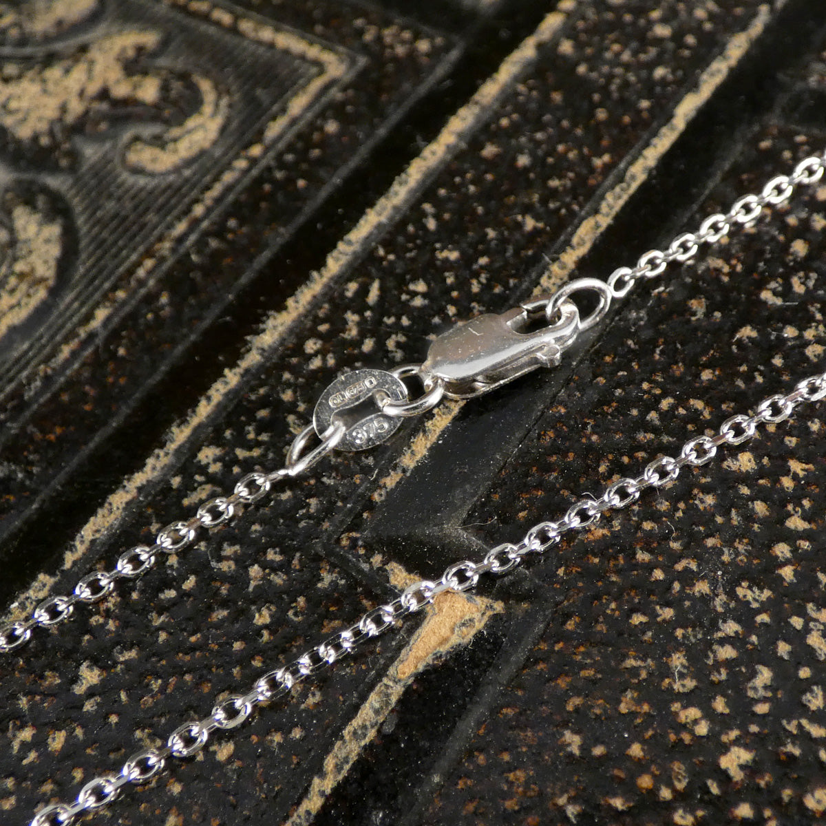 Close-up of a 9ct white gold chain on a textured black surface