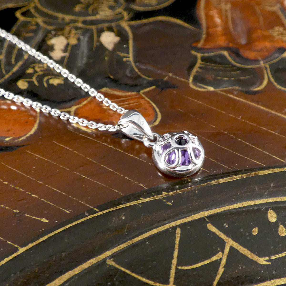 Silver pendant with purple gemstone on a chain against an ornate background