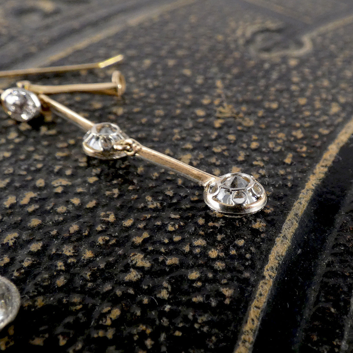 Gold earring with diamonds on a textured black surface