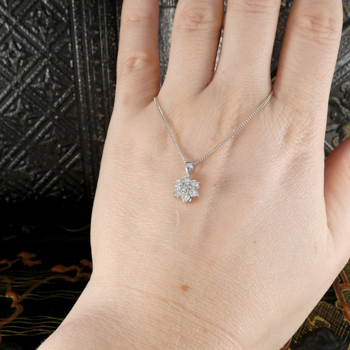 Silver necklace with a floral pendant on a hand against a dark textured background