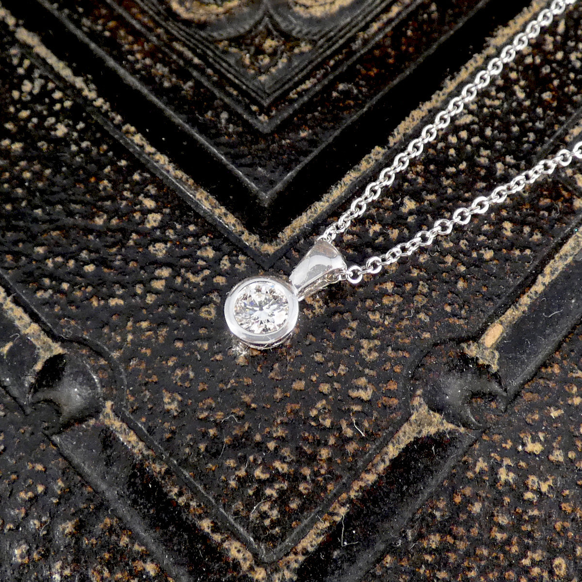 Diamond pendant on a chain against a textured black background