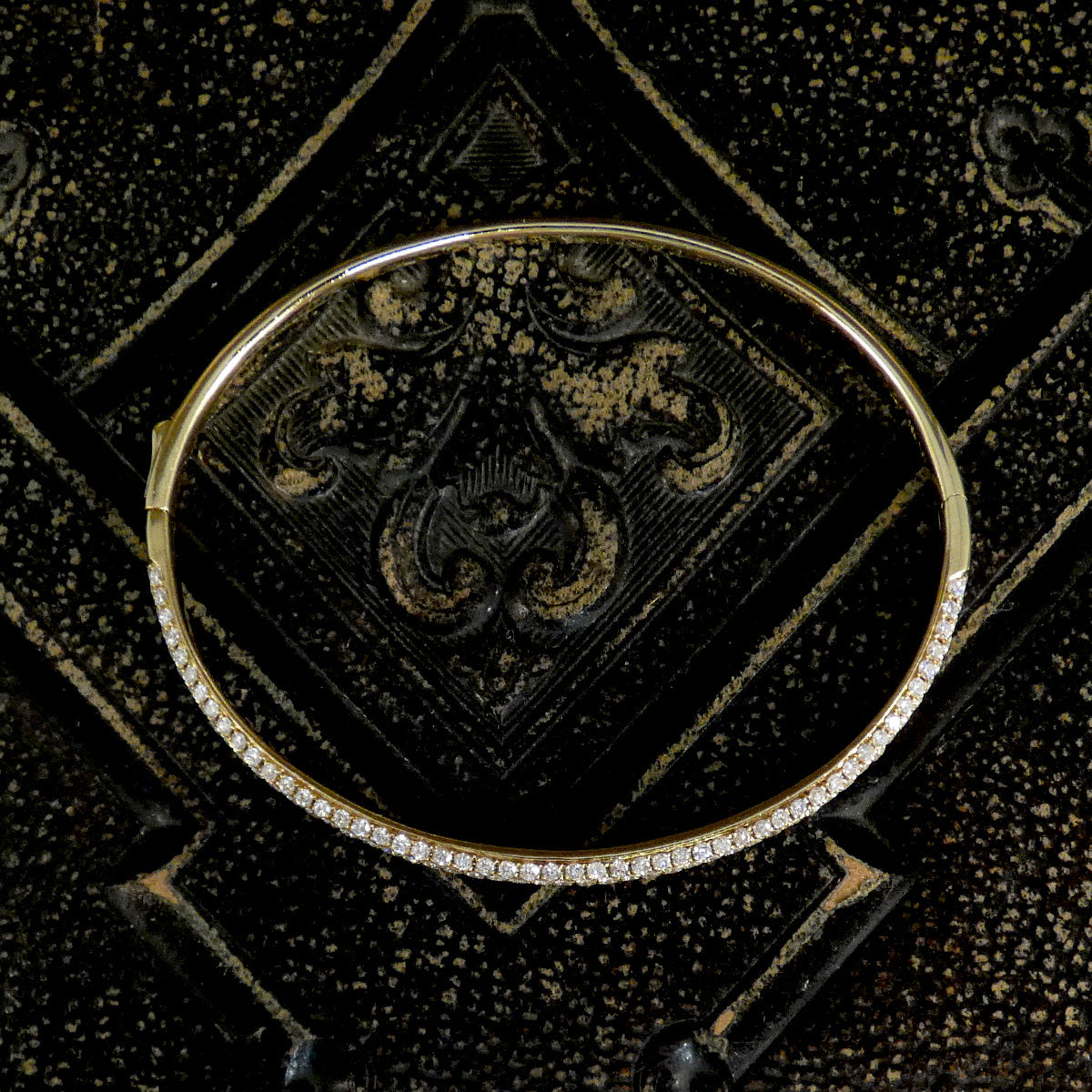Gold bracelet with diamond accents on a black textured background