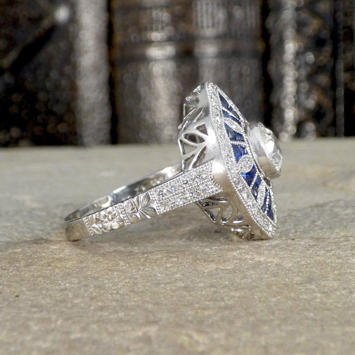 art deco style sapphire and diamond cluster ring displayed from the side showing the diamond set shoulders and floral detailing down the shoulder.