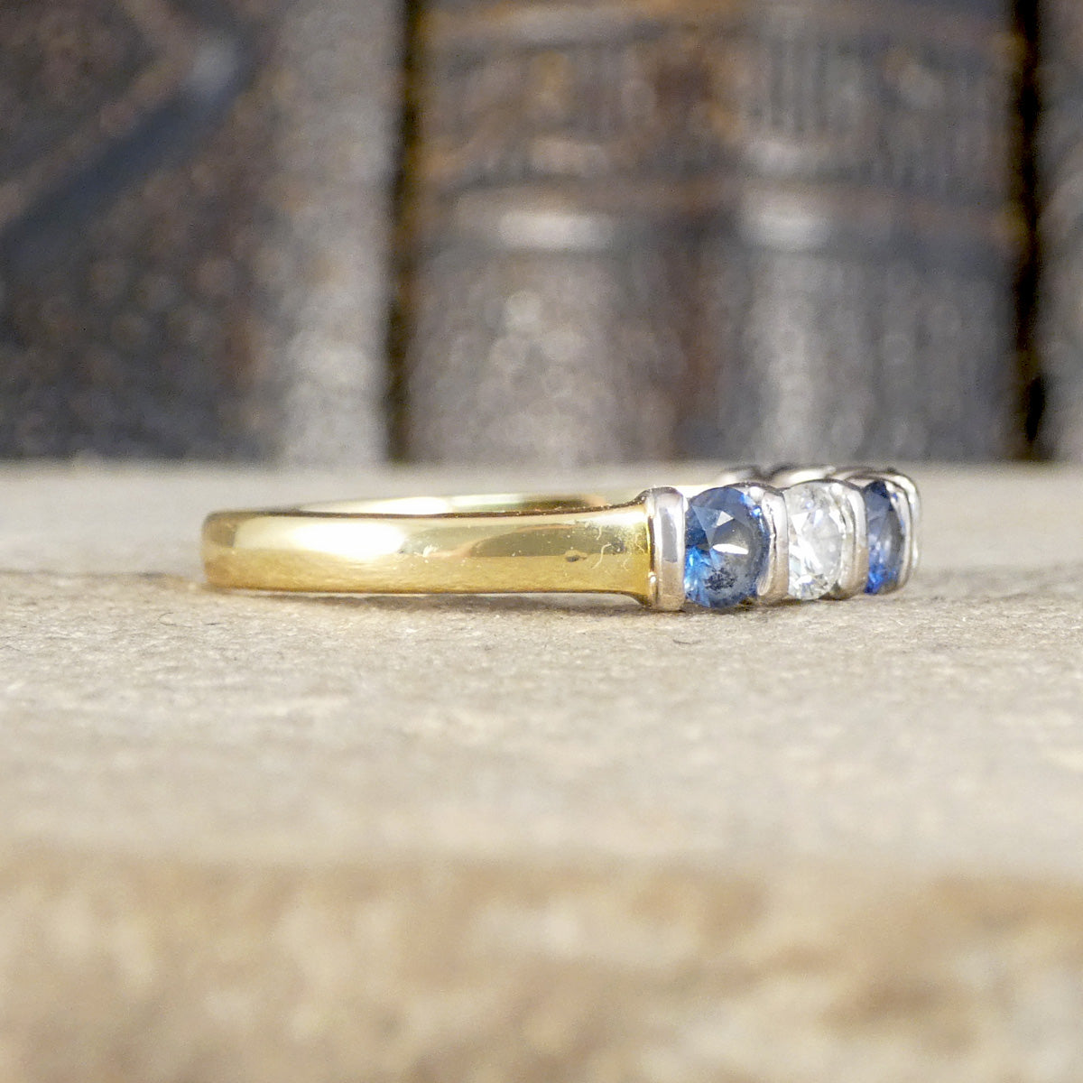 Side profile of sapphire and diamond seven stone ring with a yellow gold band.