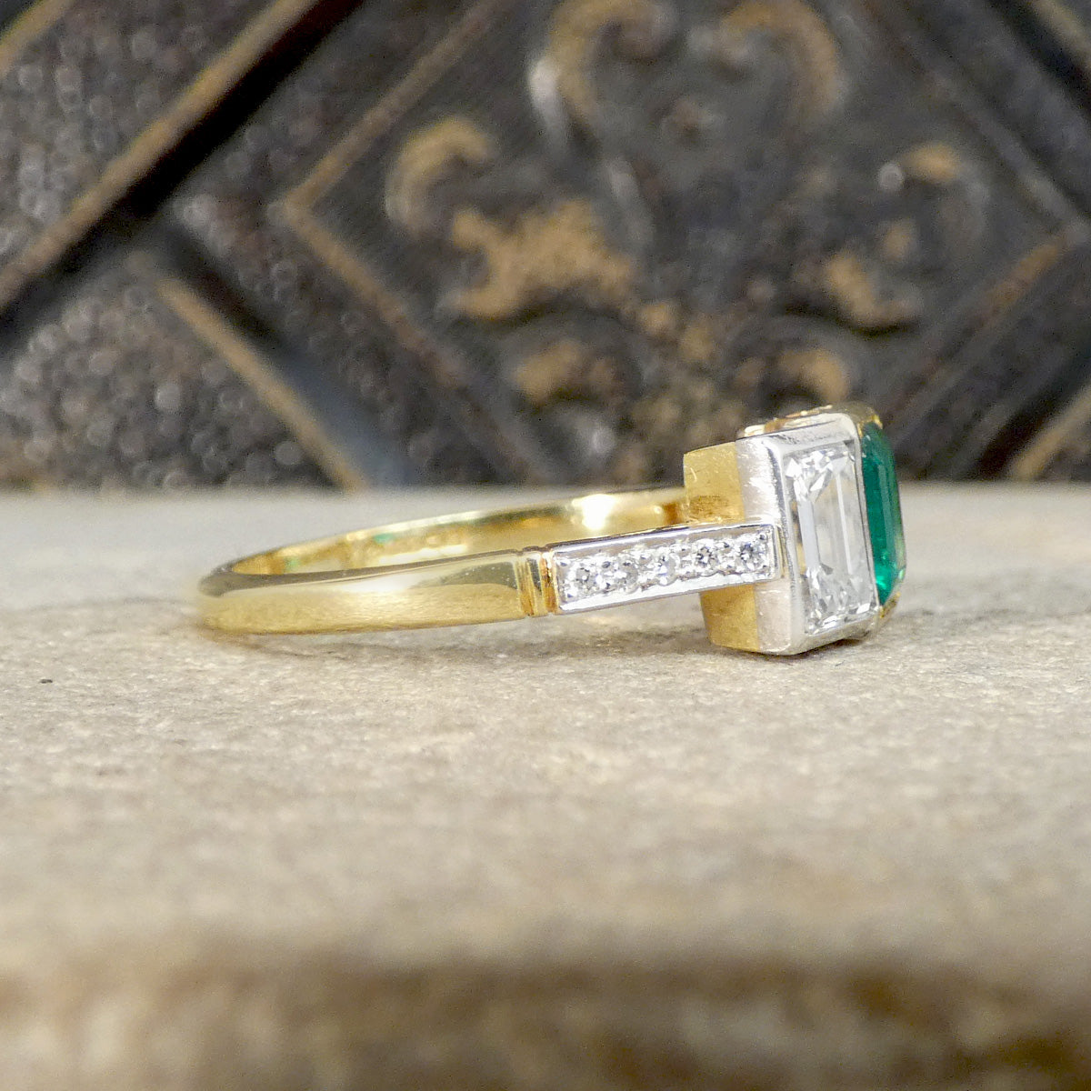 An Emerald and Diamond three stone ring in 18ct white and yellow gold. Shown from the side with diamond down the shoulders.