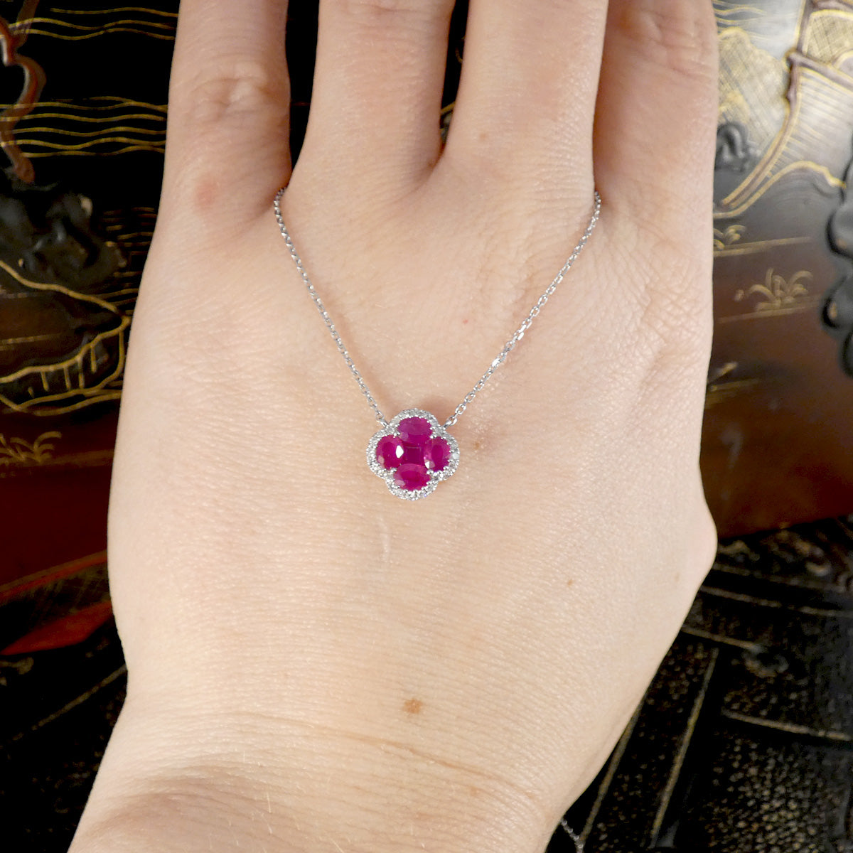 a ruby and diamond cluster necklace displayed on a hand.