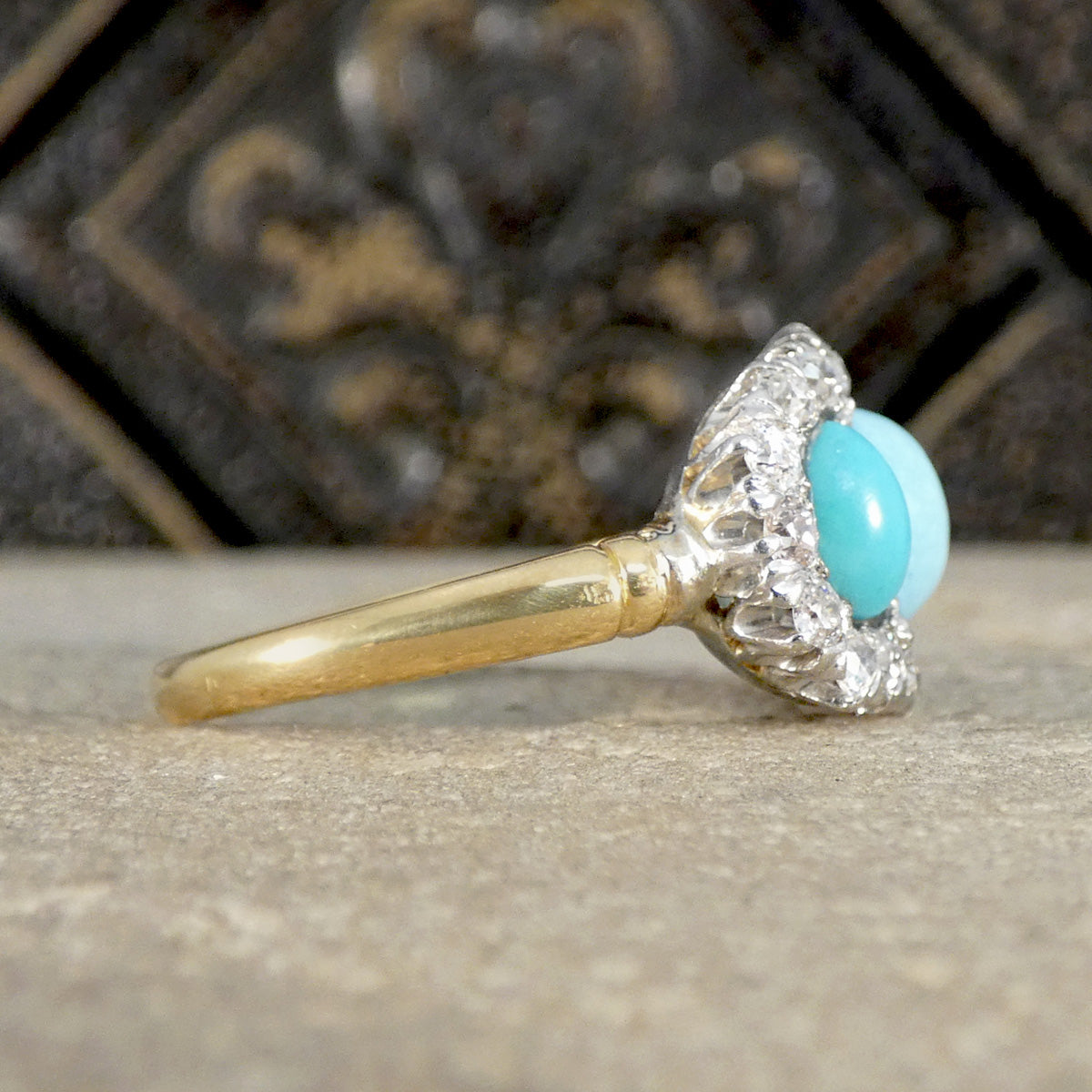 Gold ring with a turquoise stone and diamond accents on a textured surface.