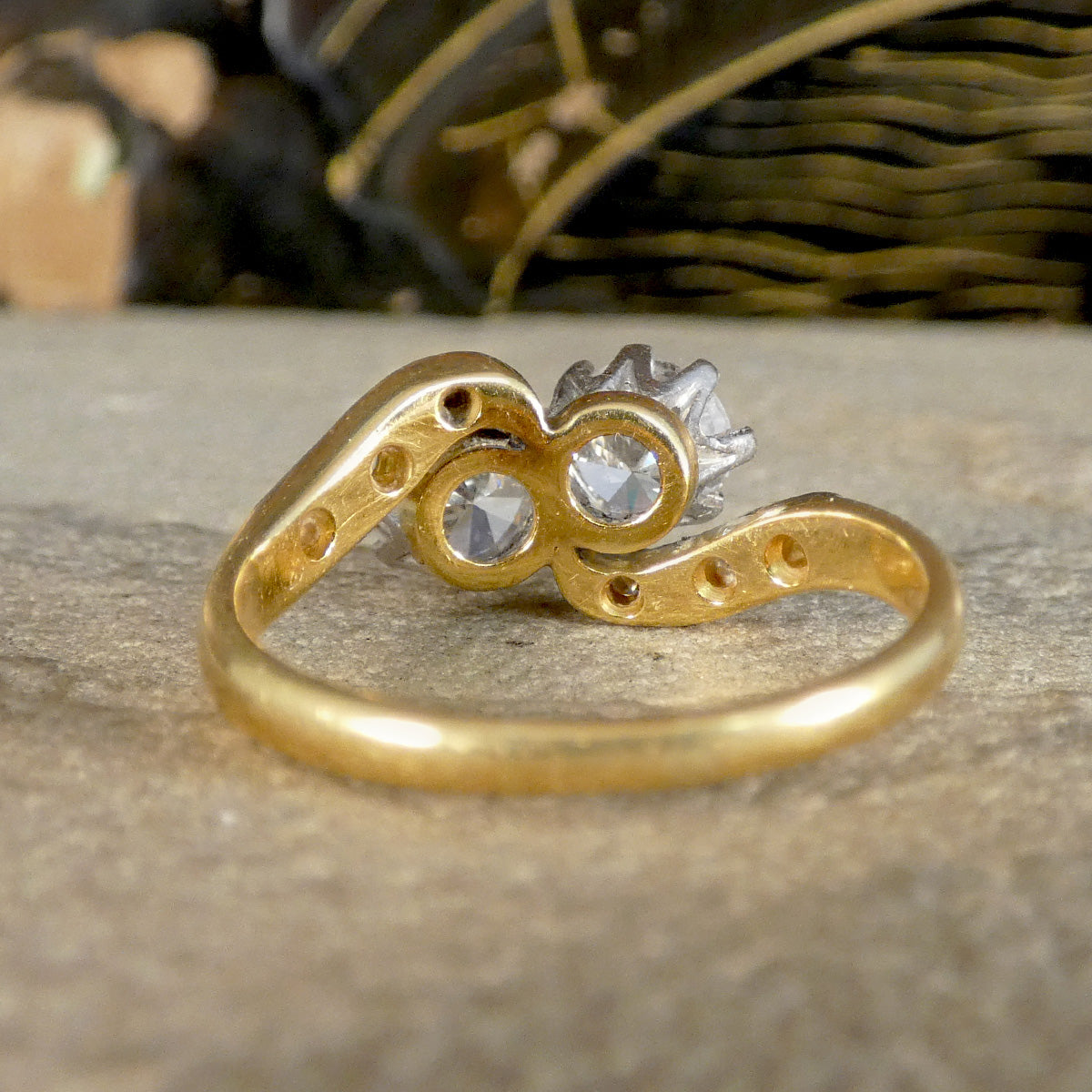 A gold ring with a unique double-loop band design and two clear gemstones, photographed close-up on a textured stone surface.