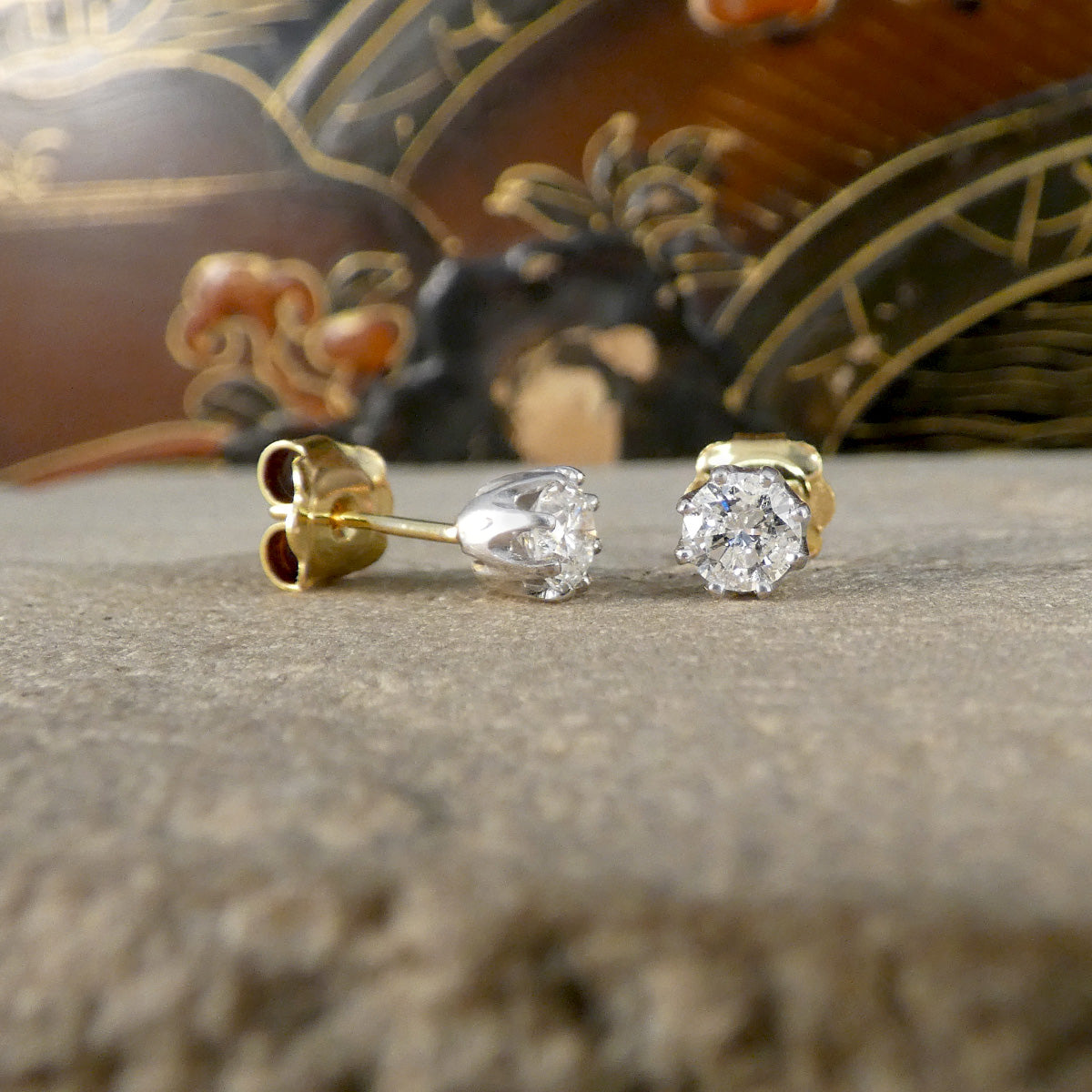Gold and diamond earrings on a textured surface with a decorative background