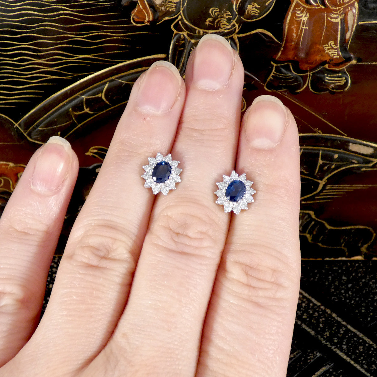 Pair of blue gemstone earrings on a hand with a decorative background