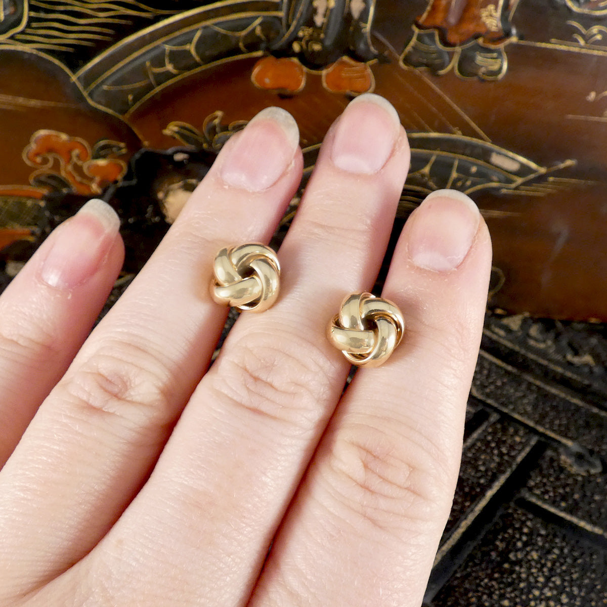 A pair of knot earrings in 9ct yellow gold displayed on a hand.