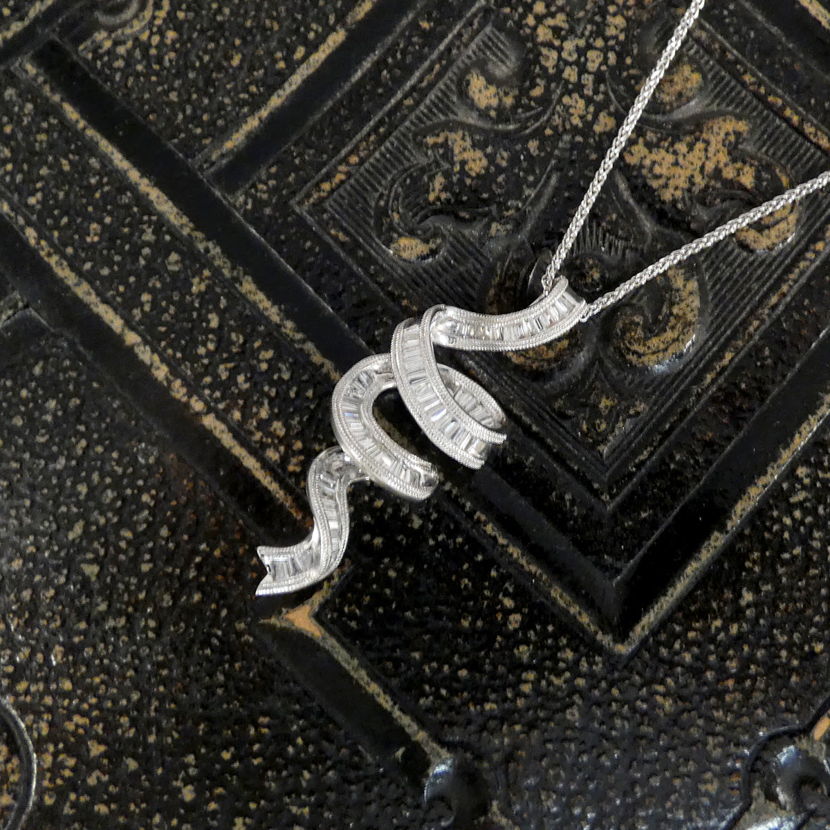 Silver necklace with a decorative pendant on an ornate black background