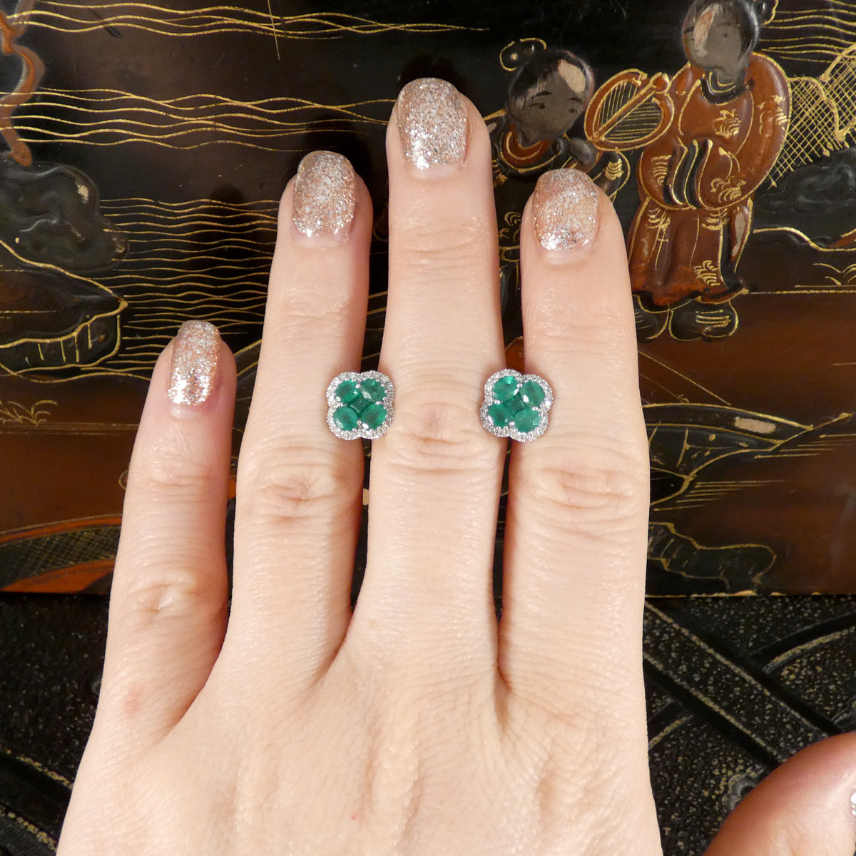 Hand displaying a pair of Emerald and Diamond clover cluster stud earrings 