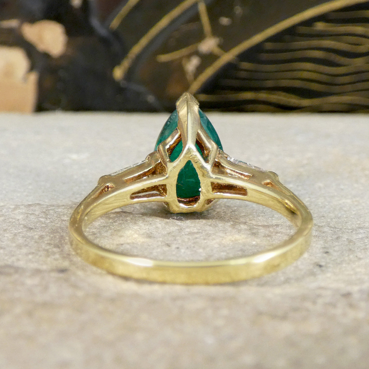 Gold ring with a green emerald gemstone on a textured surface