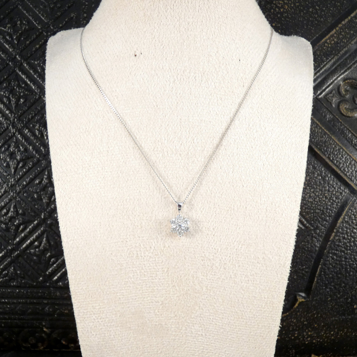 Silver necklace with a flower-shaped pendant on a mannequin bust against a textured black background