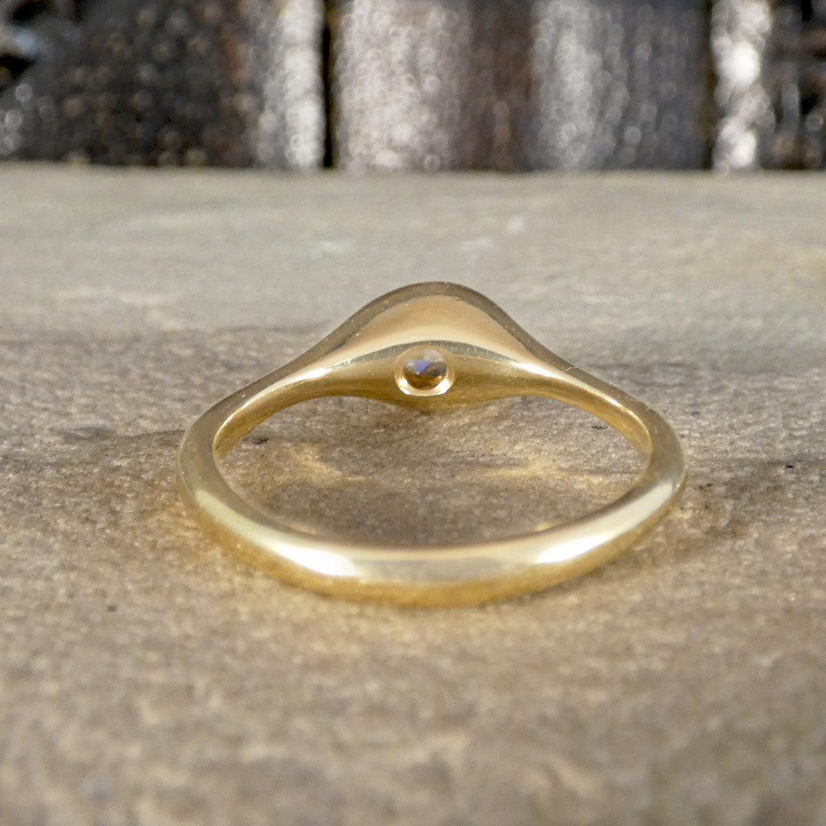 A polished yellow gold ring with a small round clear gemstone in the center of its dome-shaped head, resting on a textured stone surface.