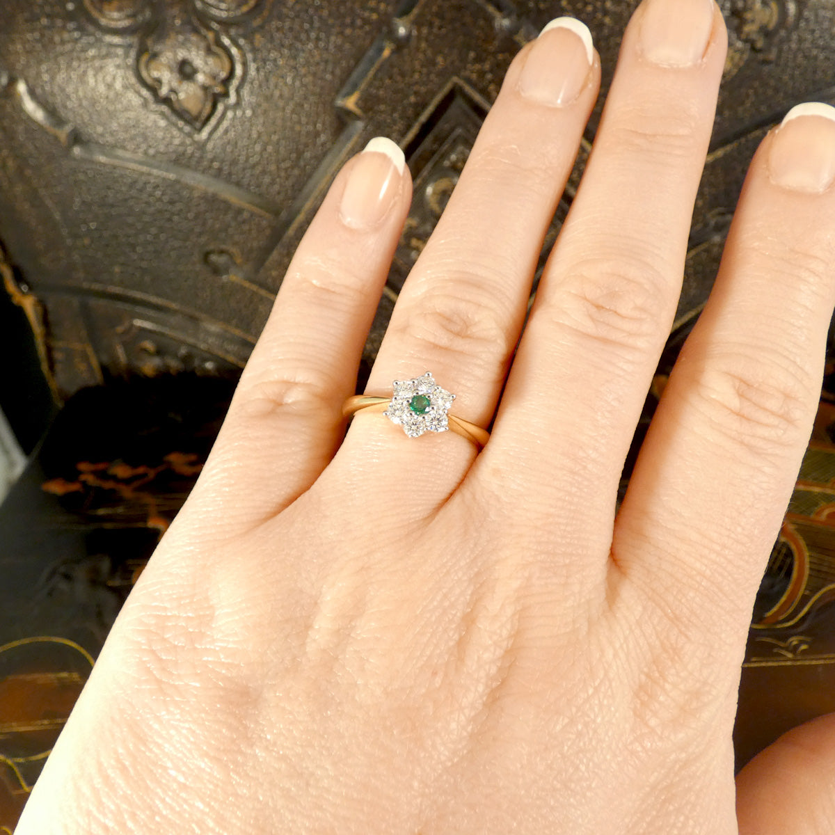 An Emerald and Diamond flower cluster ring in 18ct Yellow and White Gold. Displayed on the hand to see size and colour reference. 