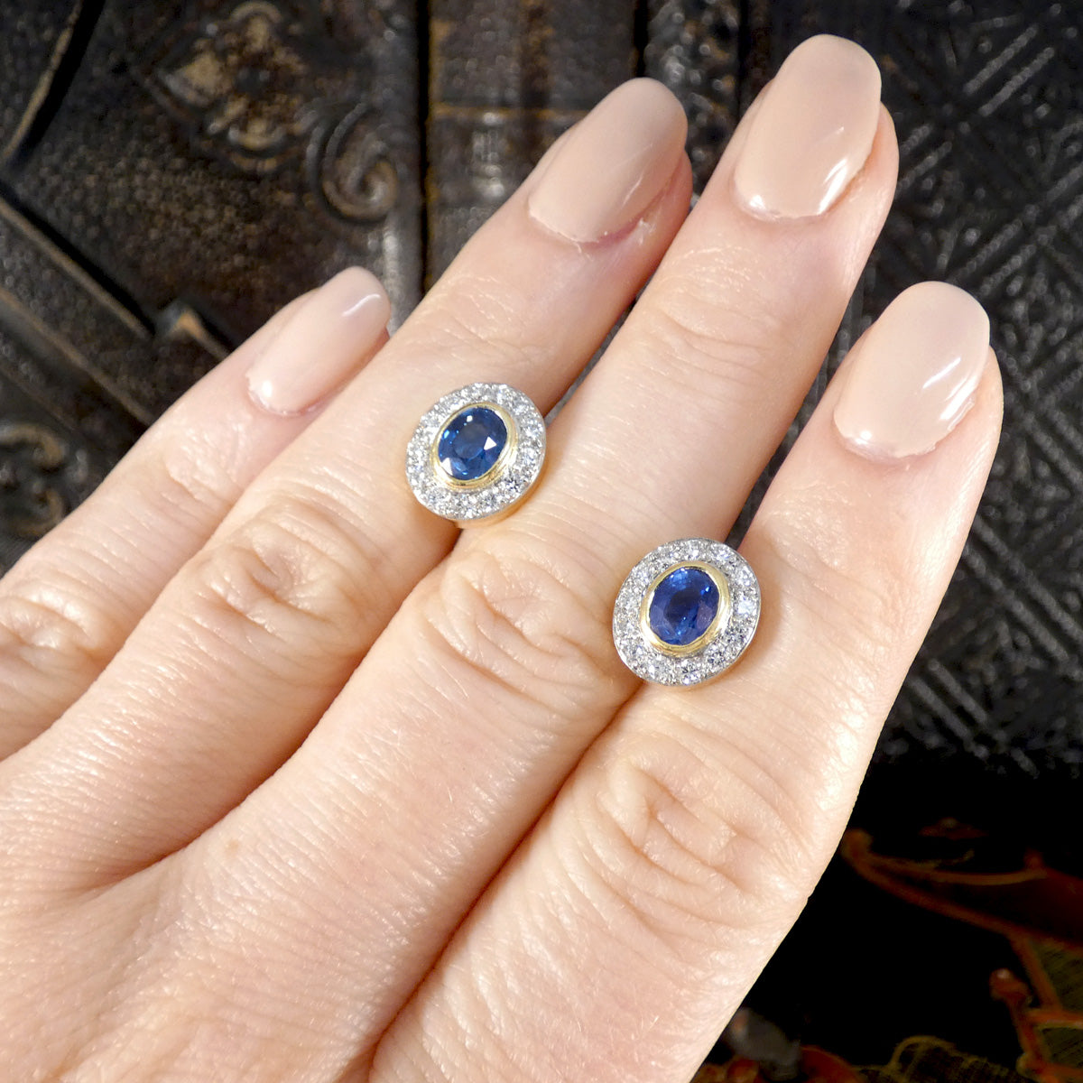 A beautifully bright pair of sapphire and diamond stud earrings in 18ct gold with a bezel setting. Shown on hand to see size and colour reference. 