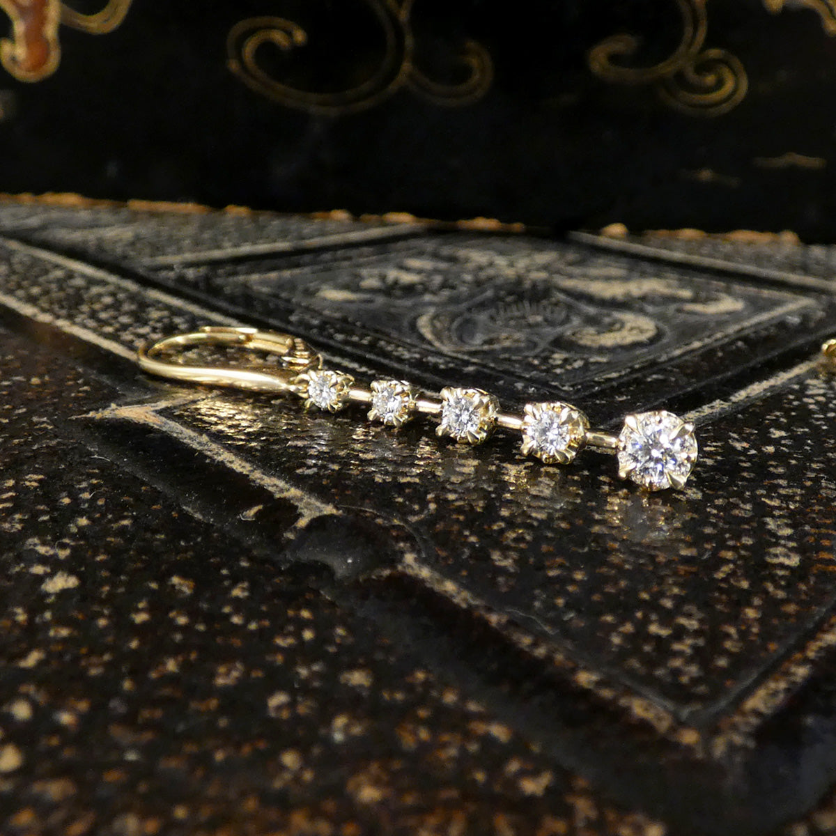 A gold key ring with four round-cut clear gemstones in a row, resting on a textured dark brown leather surface.