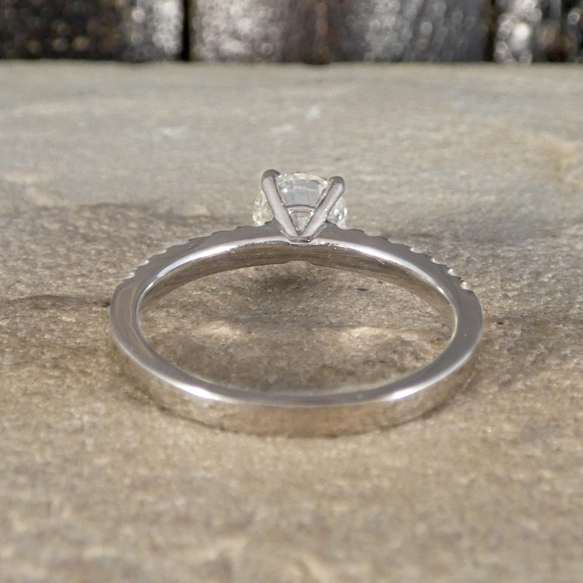 An 18ct white gold solitaire engagement ring with a round clear gemstone, resting on a textured stone surface.