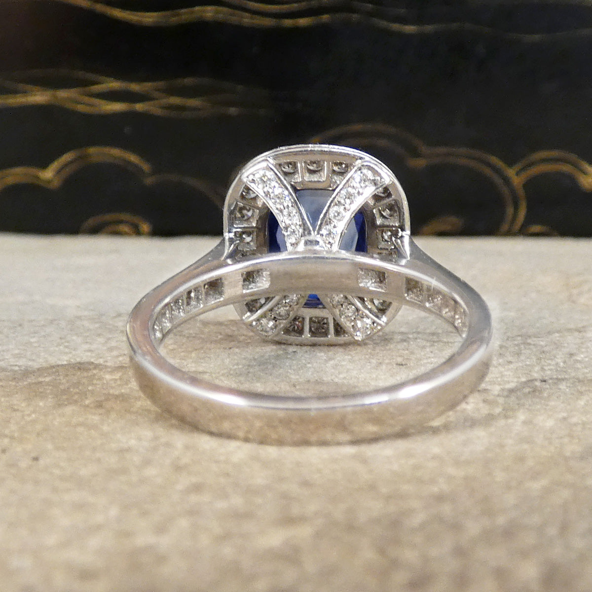 A sapphire and diamond cluster ring with a diamond set shoulder and wedfit appearances and diamonds set under the bezel.