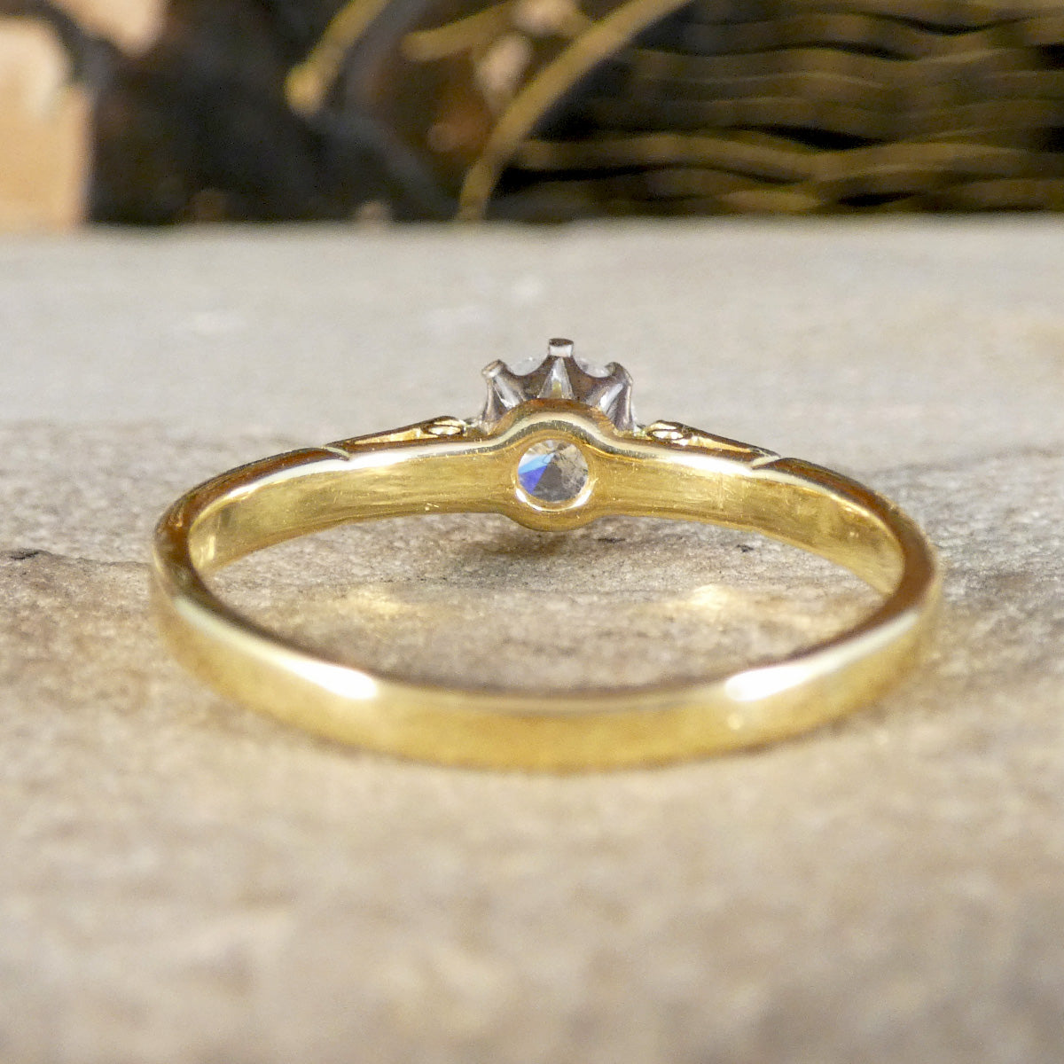 A yellow gold ring with a small crown-like setting and a central round clear gemstone, resting on a textured stone surface.