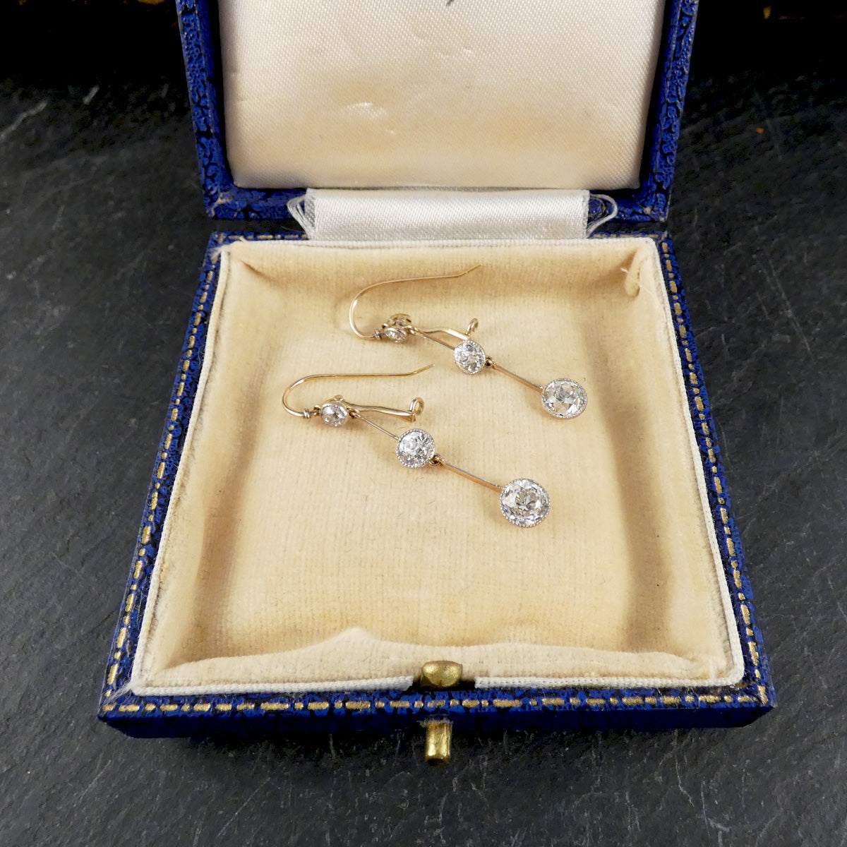 Pair of gold and diamond earrings in a blue jewelry box on a dark surface
