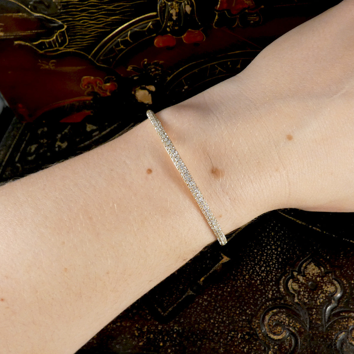 diamond set gold bracelet on a wrist with an ornate background